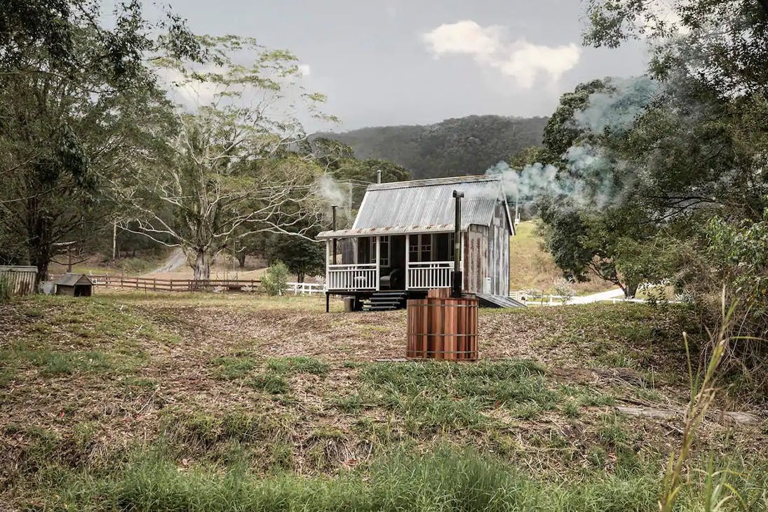small rustic looking house in the bush with a spa outside